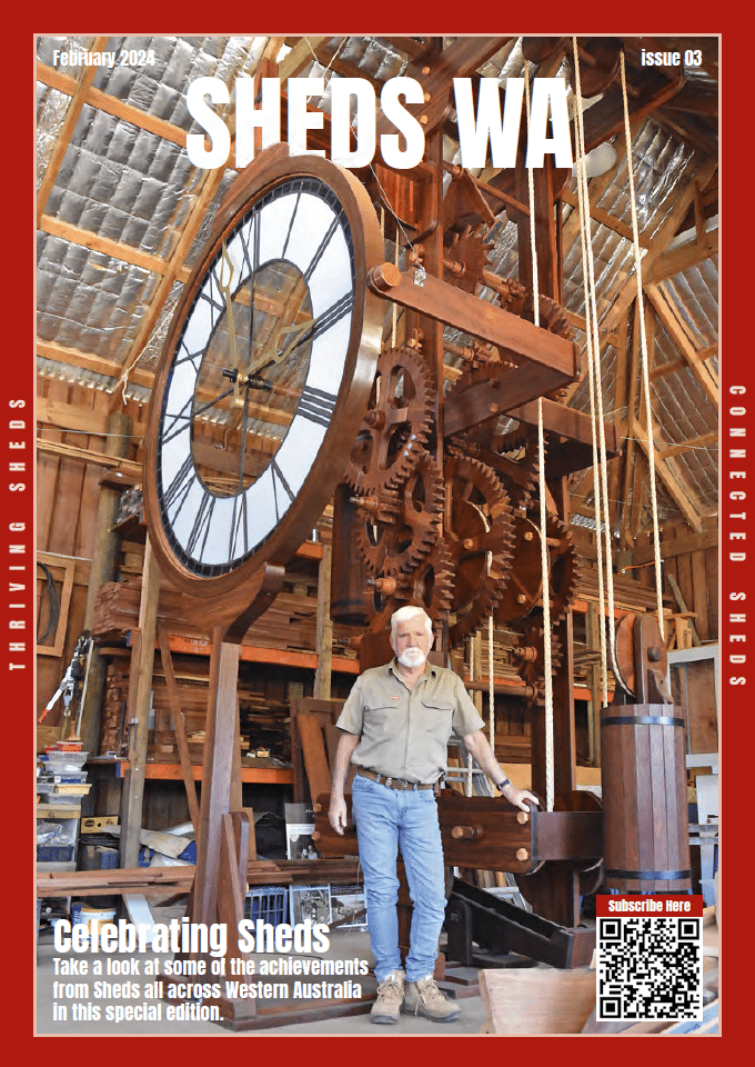 Image of man (Kevin Bird) standing in front of 6 metre tall wooden clock inside a shed.